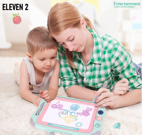 A mom and her son playing on a magnetic drawing board. The son is looking at what his mom is drawing. There's a house, tree, sun, and some plants already drawn.