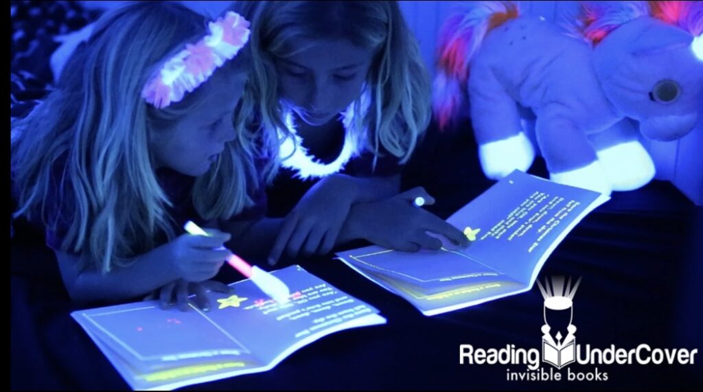 Two children reading books with invisible ink and pen that has UV lighting attached to it. 