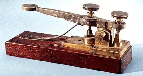 A wooden machine, looks a little like a sewing machine. Consists of a sturdy base supporting a key for inputting messages. A sounder produces audible clicks in response to received electrical signals, helping decode Morse code. 