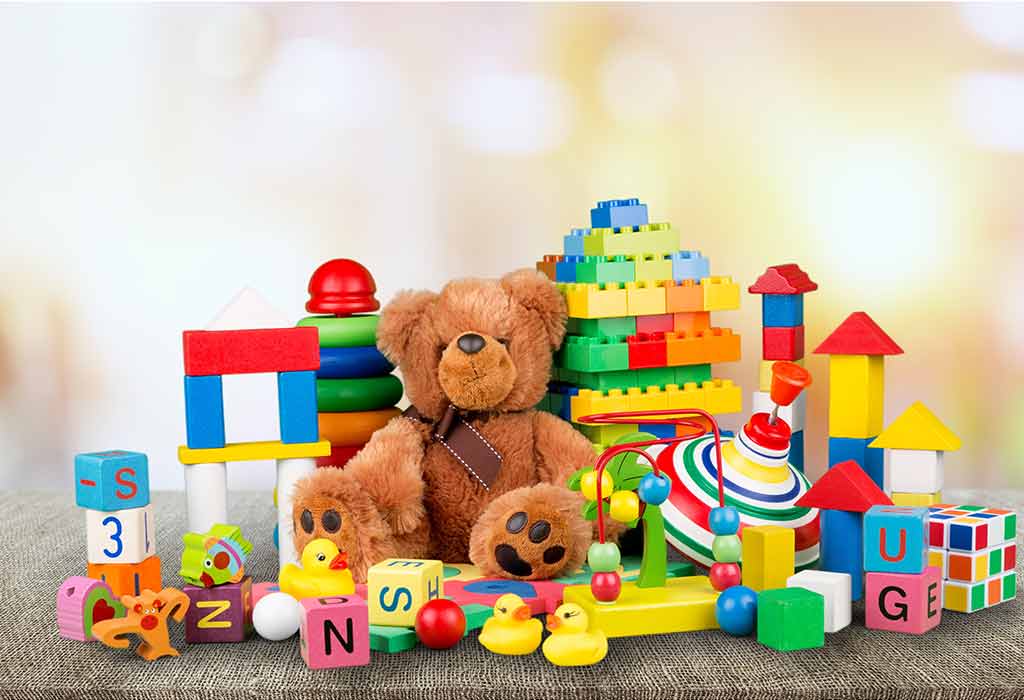 A collection of toys for kids. There are some learning bocks, a brown teddy bear, legos, and so on. The toys are on the floor with a faded background so the focus is completely on the toys. 