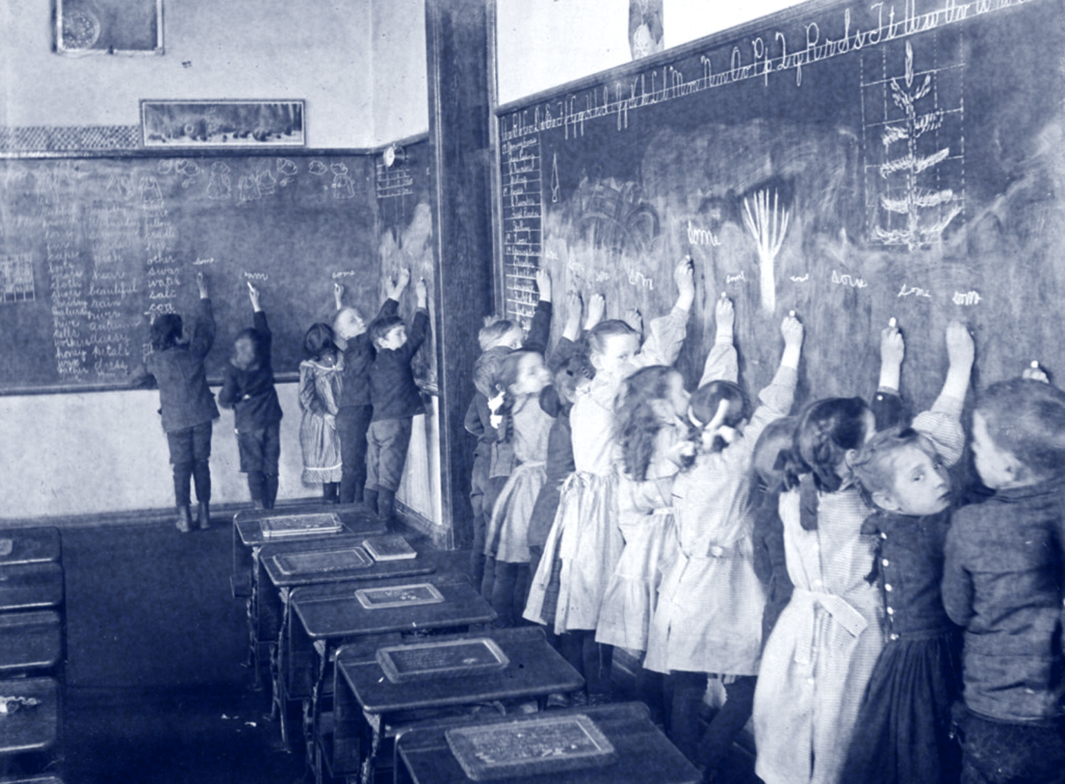 This image shows a group of students writing on a chalkboard in a classroom. 
