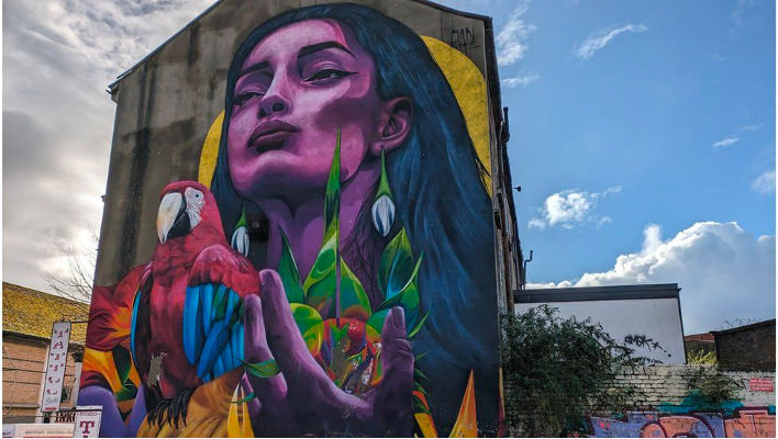 A colorful mural of a young purple woman's face and a parrot in her hand. 
